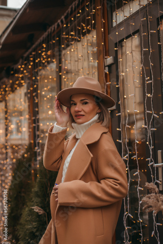 Outdoor fashion portrait of an elegant woman in a beige hat and coat posing in a european city.