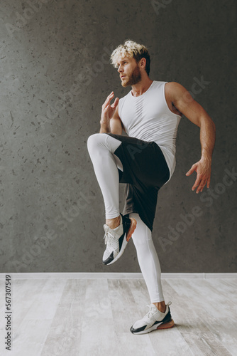 Fototapeta Naklejka Na Ścianę i Meble -  Full body sideways young strong sporty athletic sportsman man wearing white tank shirt black shorts training do exercise for legs running start warm up training indoor at gym. Workout sport concept.