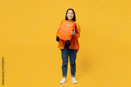 Young woman wears summer casual clothes stand hold in hand suitcase valise isolated on plain yellow background. Tourist travel abroad in free spare time rest getaway. Air flight trip journey concept. #567308355