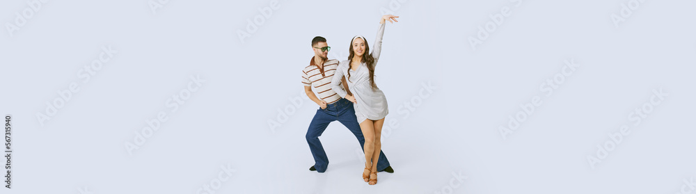 Young beautiful girl in silver dress and stylish man dancing disco dance isolated over grey studio background. 70s fashion, hobby, hippie lifestyle, American culture. Copy space for ad, text. Banner Young beautiful girl in silver dress and stylish man dancing disco dance isolated over grey studio background. 70s fashion, hobby, hippie lifestyle, American culture. Copy space for ad, text. Banner