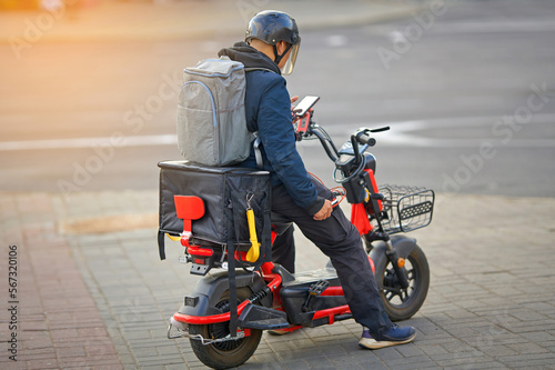 Online delivery service  delivering food with e-scooter. Courier rides electric moto bike  deliver food orders to customers. Boy in helmet ride electric scooter with thermal box  fast food delivery.