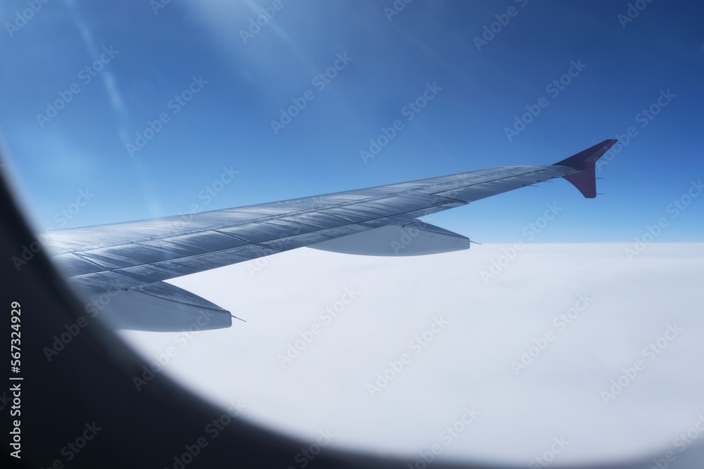 Aircraft wing amidst cloudy sky seen through window