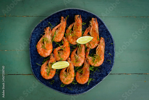 Shrimp sauteed with garlic and oil in a dark blue dish on a green painted wooden table. Brazilian food widely consumed on the coast.