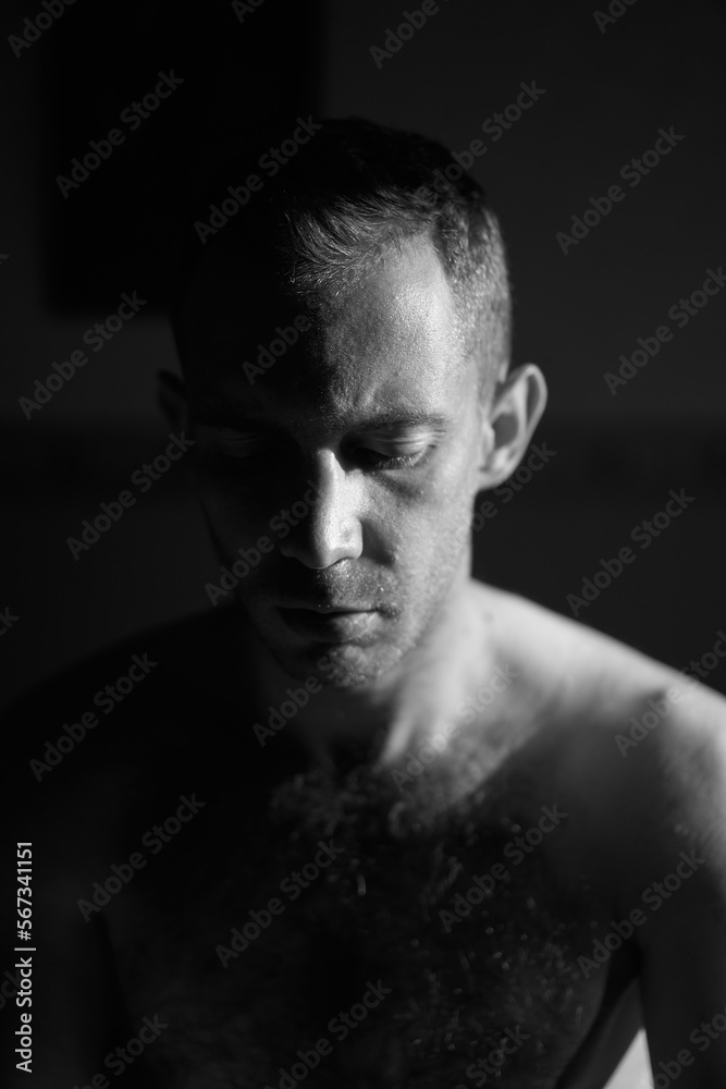 Portrait of handsome man in hard side light meditating. Half of male face lit by the sun rays on sunrise. Self reflection and depression concept. Calming place for meditation and spiritual prayer.