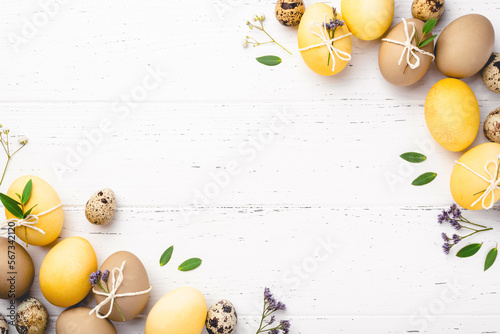Festive Easter background. Yellow and brown Easter Eggs with flowers on a white wooden table. Greeting card with place for text. Top view.