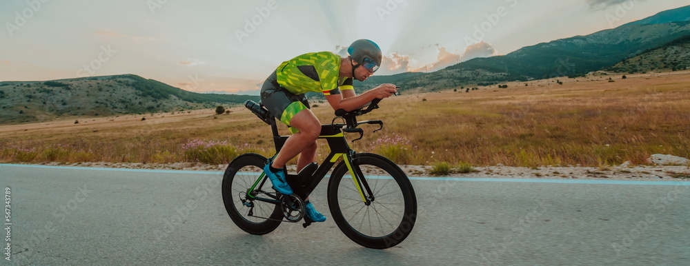 Fototapeta premium Full length portrait of an active triathlete in sportswear and with a protective helmet riding a bicycle. Selective focus 