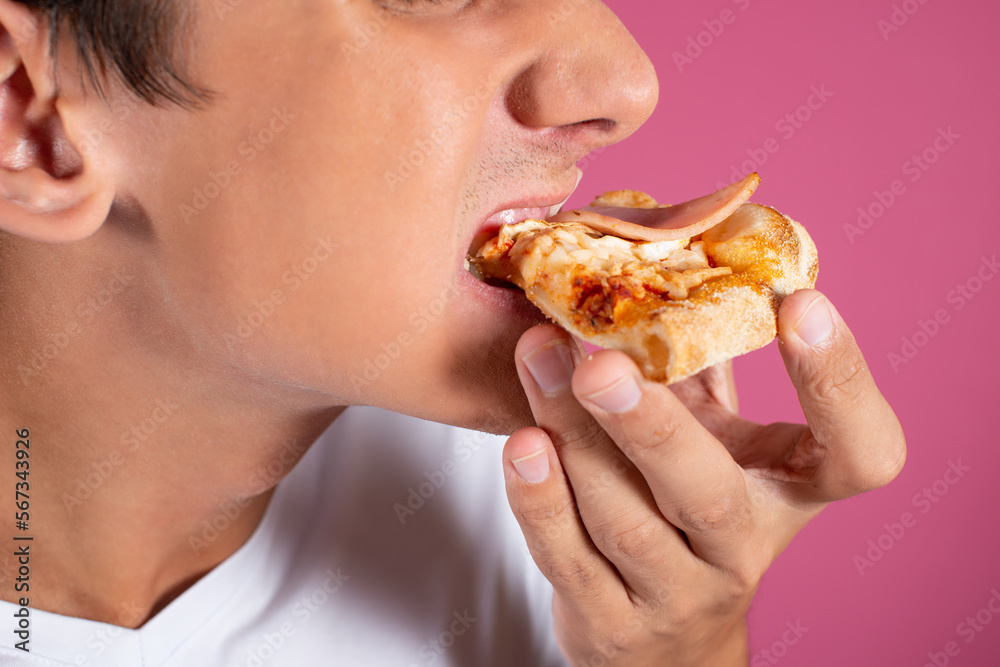 Portrait of a hungry guy in a white shirt with a piece of pizza. Pink background. Fast food. Portrait of a hungry guy in a white shirt with a piece of pizza. Pink background. Fast food.