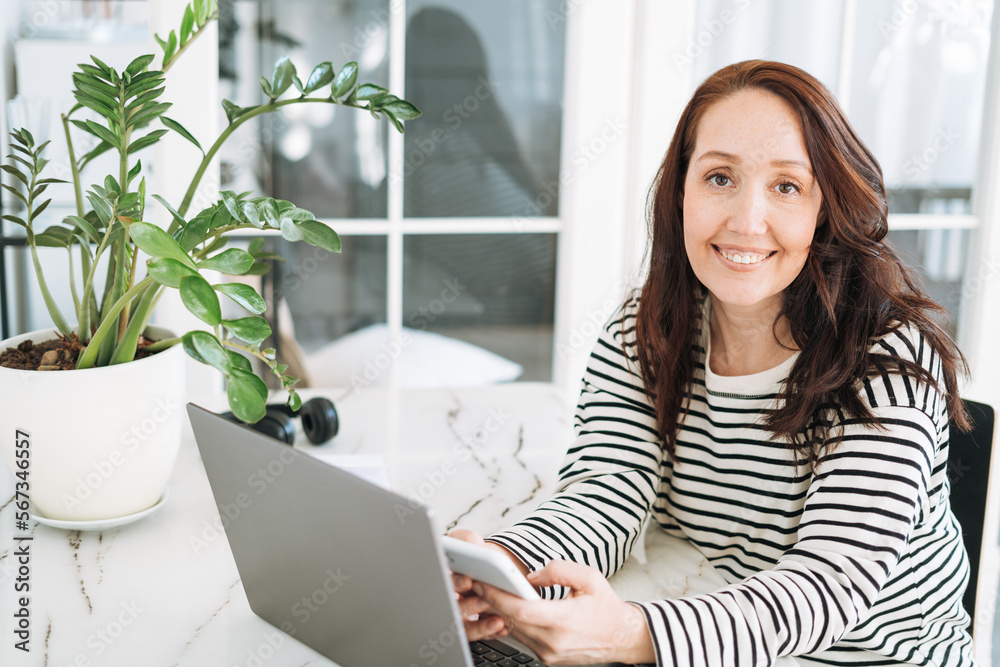 Smiling brunette woman in casual clothes working at laptop in bright modern office