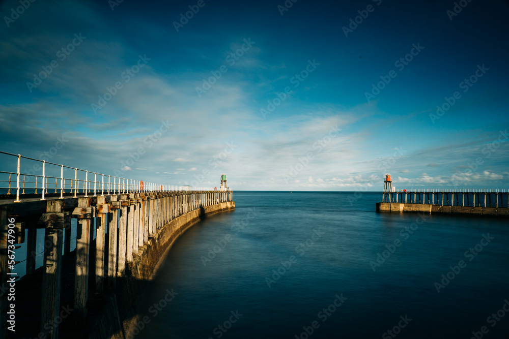 Fototapeta premium Whitby Harbour pier with lighthouse and wooden boards with metal railings and the sea in the background.