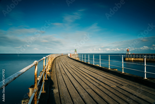 Whitby Harbour pier with lighthouse and wooden boards with metal railings and the sea in the background.