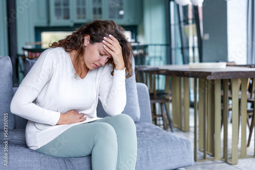 Young woman sitting on the couch at home with a pain in her stomach