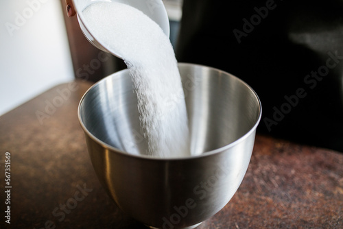 sugar is poured from a small bowl into a large steel container
