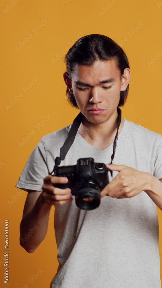 Vertical video: Young professional photographer using dslr camera to take pictures, having fun with photos at photography shoot in studio. Male model posing with equipment, feeling confident. Vertical video: Young professional photographer using dslr camera to take pictures, having fun with photos at photography shoot in studio. Male model posing with equipment, feeling confident.