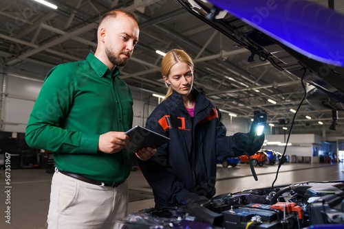 The manager, together with a young female car mechanic, performs diagnostics under the hood of the car. Modern professional service station equipment
