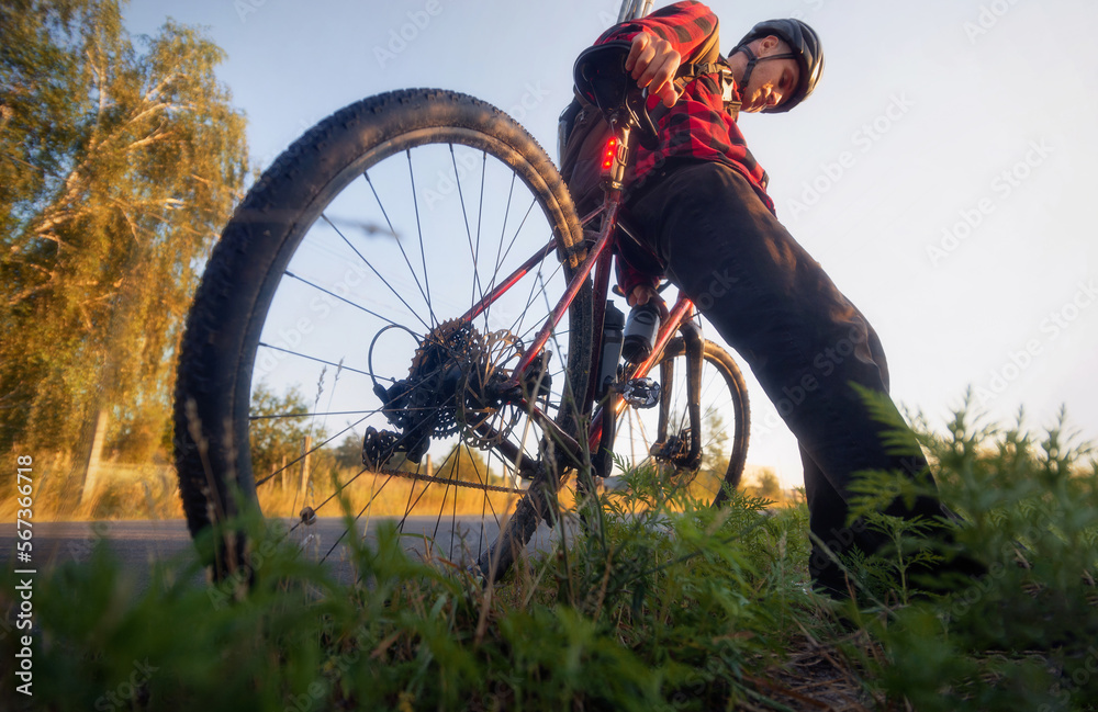 Obraz premium Cyclist sits on his bicycle nearby the road at sunny morning. Low angle view. Sport concept.