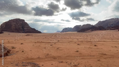 Panoramic view of Wadi Rum desert in Jordan with clouds moving over flat sand landscape with mountains in background,