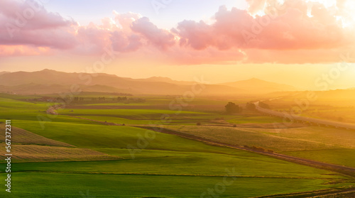 beautiful sunset or sunrise in rural countryside green hills with farm and mountains on background