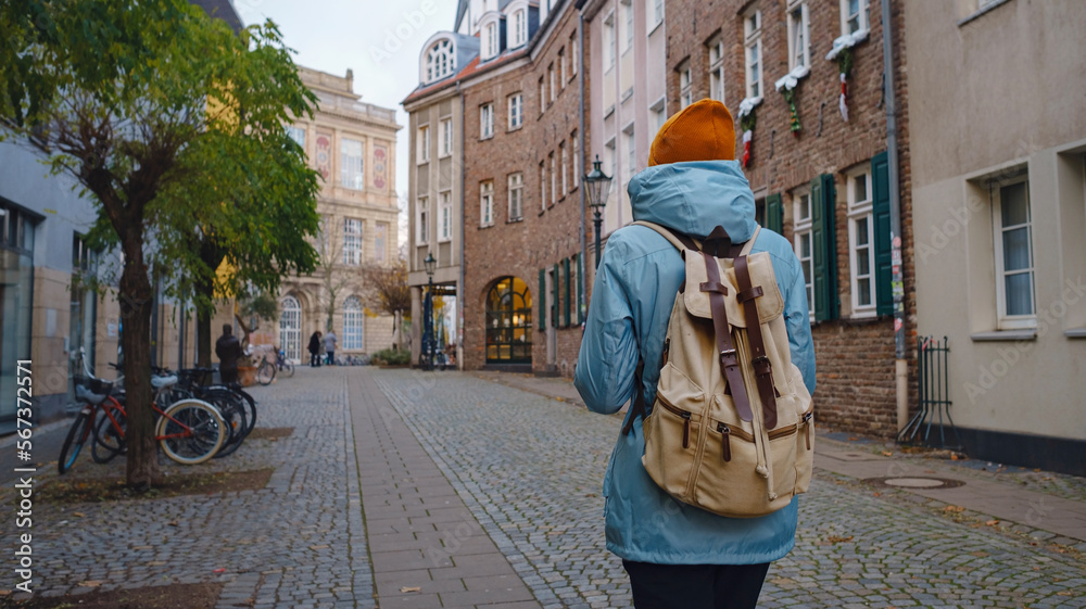 winter travel to Dusseldorf, Germany. young Asian tourist in blue jacket and yellow hat (symbol of Ukraine) walks through sights of old town or Altstadt. Popular center of Rheinland and Westphalia