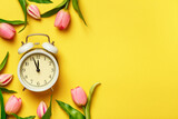 Alarm clock surrounded by tulips. Transitional change of time, change of seasons. copy space