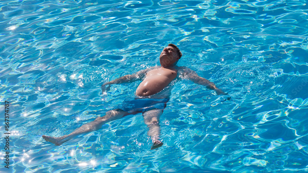 An adult large man swims his back in a pool with clear blue water.