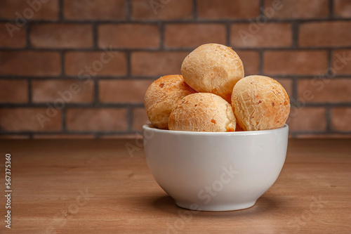 Cheese breads in a white bowl on wooden table and bricks wall background.