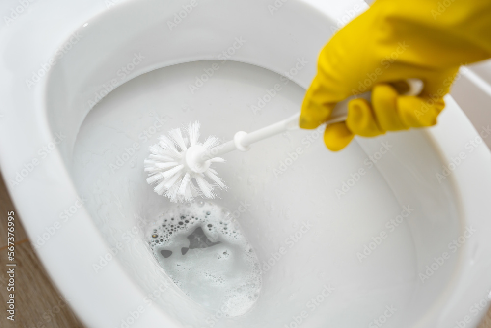 Cleaning and disinfection of toilets. Cleaner in yellow rubber gloves cleans the toilet with a brush Cleaning and disinfection of toilets. Cleaner in yellow rubber gloves cleans the toilet with a brush
