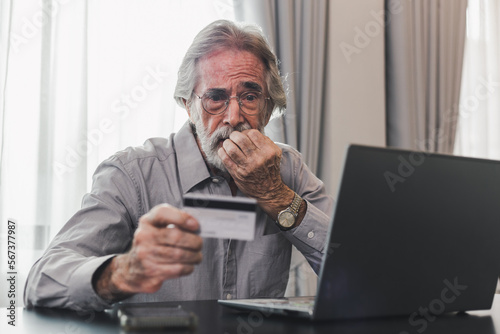 Upset senior elderly man holding credit card by laptop having trouble worry finance safety data or online payment security. Bank client concerned about problem with credit card, financial fraud threat