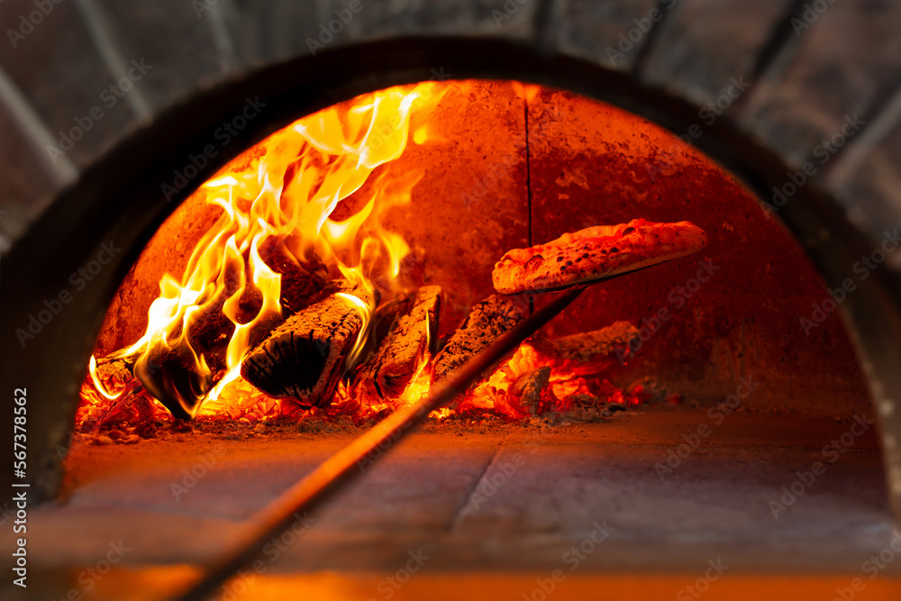 Italian pizza is cooked in a wood-burning oven. The cook puts the pizza in the oven on a shovel.