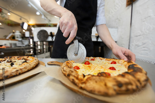 Close-up of the chef-baker's hand cutting pizza in the restaurant kitchen.
