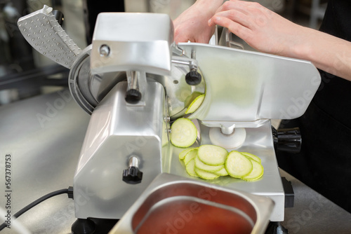 The chef in the restaurant kitchen prepares zucchini slices with a slicer.