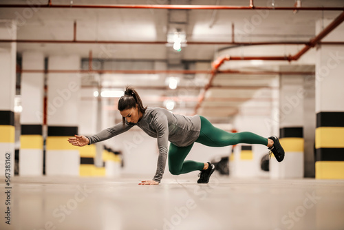 A strong sportswoman is doing strength exercised in underground garage.