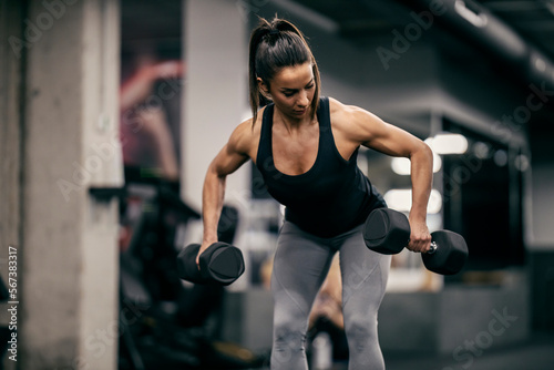 A sportswoman is lifting dumbbells during her strength training in a gym.