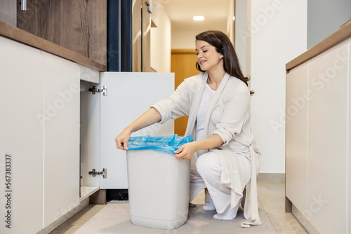 A neat pregnant woman is changing trash bag and putting new one in a bin at home.