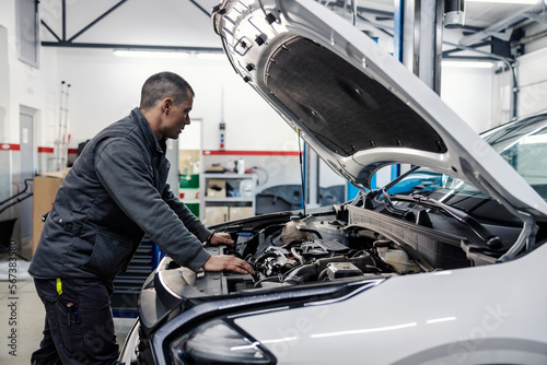 A mechanic is looking under the car hood and fixing it at mechanic's shop. photo