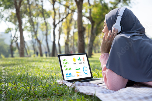 Muslim woman listening music laying on grass at park with laptop after learn growth plants on infographic in her screen. Freelancer female working and Educator for environments and earth concept