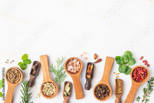 Various spices and green herbs in wooden spoons on white table