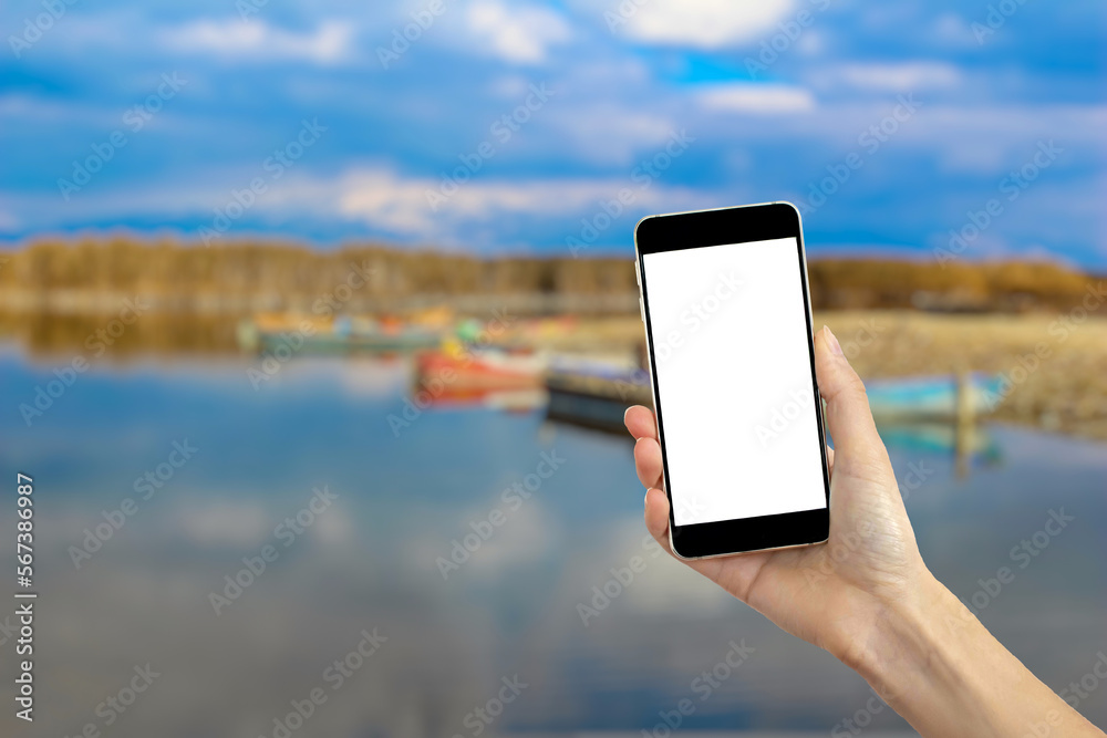 Hand holding mockup phone, blurry lake view in the background