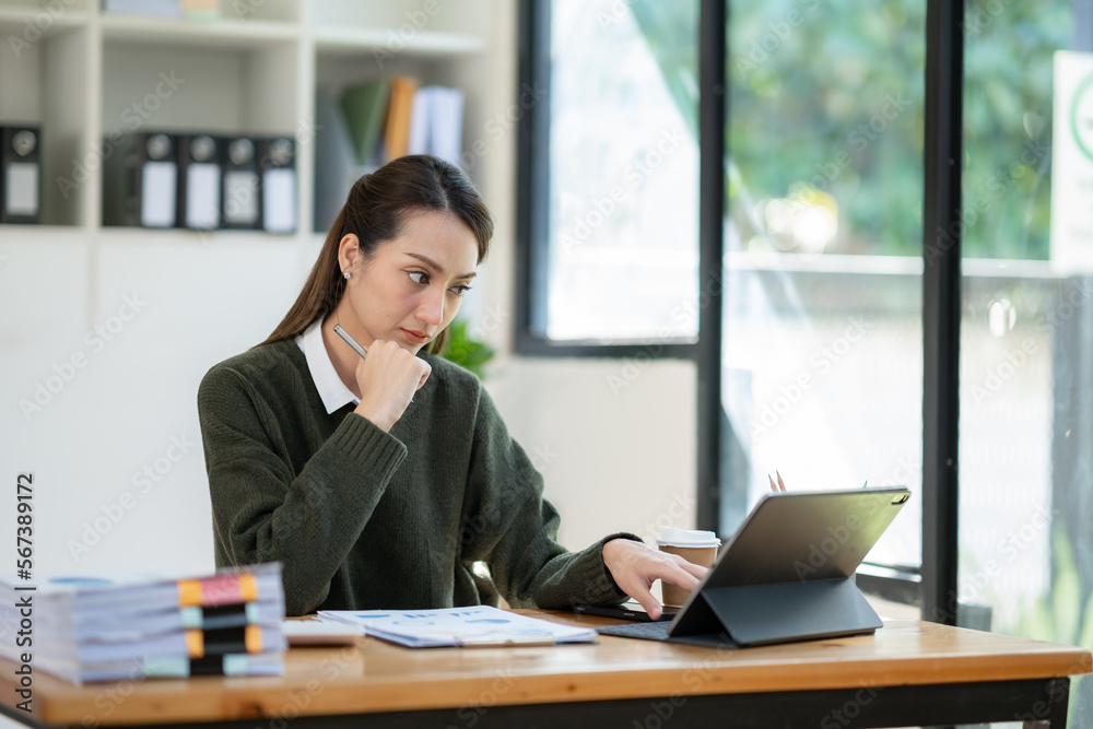 Young Asian businesswoman holding a pen sitting and analyzing the details of management information Finance is happy at the desk in the office. Young Asian businesswoman holding a pen sitting and analyzing the details of management information Finance is happy at the desk in the office.