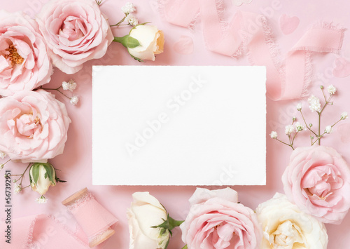 Blank paper card between pink roses and pink silk ribbons on pink top view, wedding mockup © katrinshine