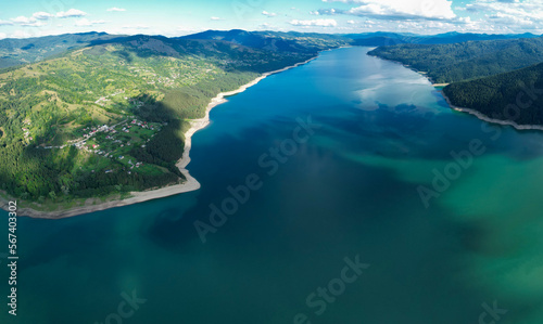 Aerial drone panorama above Izvorul Muntelui Lake. Sunny summer evening. Clouds are casting shadows above the lake and the nearby small villages and tourists resorts. Ceahlau Mountains  Carpathia.