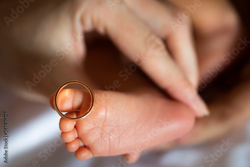 Golden wedding rings on tiny newbornbaby's feet and toes in hands or palms of new parents, mom and dad 