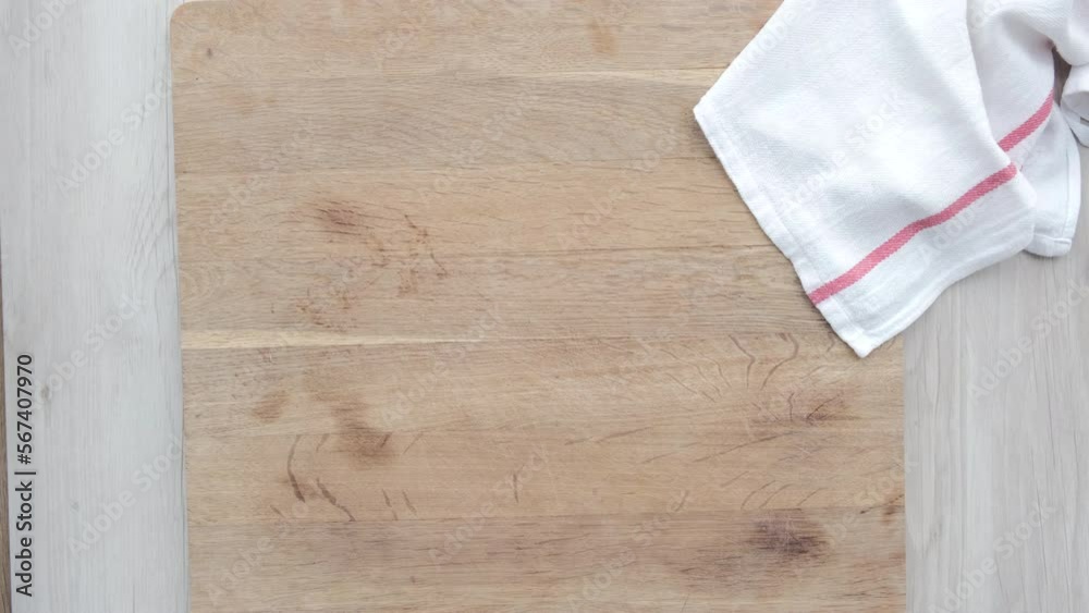 Mano de mujer coge dos berenjenas de una tabla de madera con paño blanco y rojo