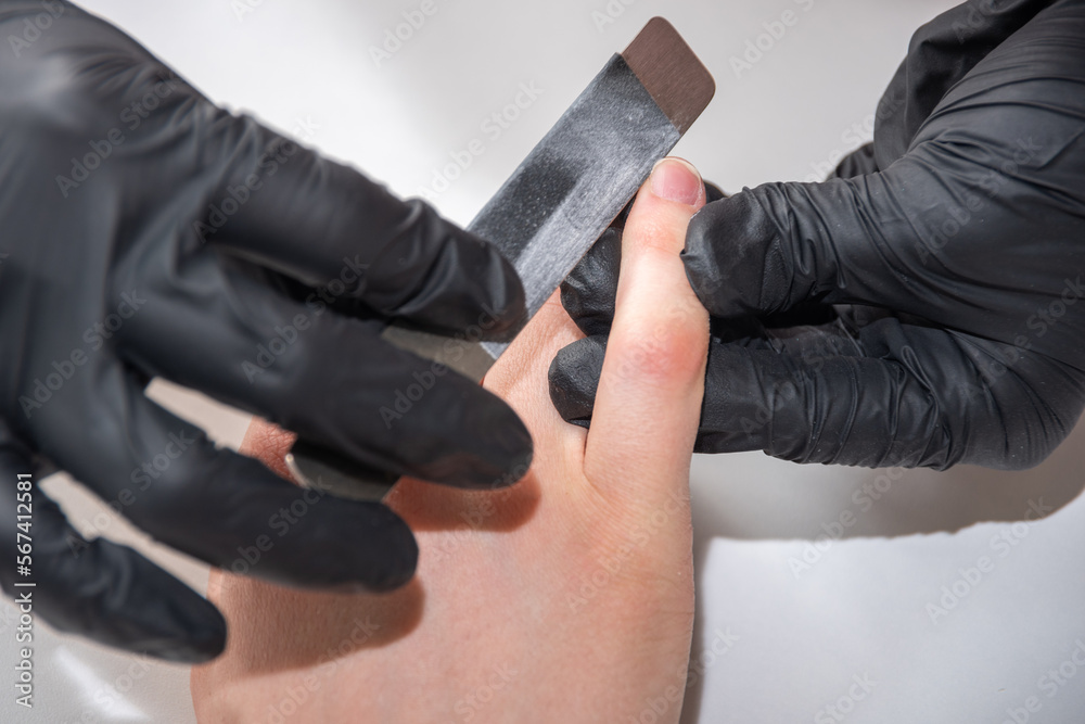 Gloved hands of a skilled manicurist filing a young woman's nails with a nail file. Hands during a manicure care session