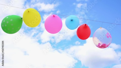 Wind blows the colorful party balloons, in the background is the blue sky with clouds.
