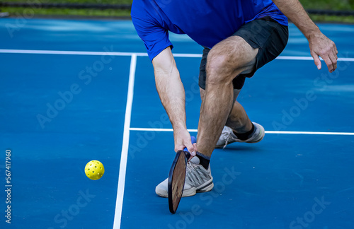 Male pickleball player digs deep to scoop up the ball off the court surface photo
