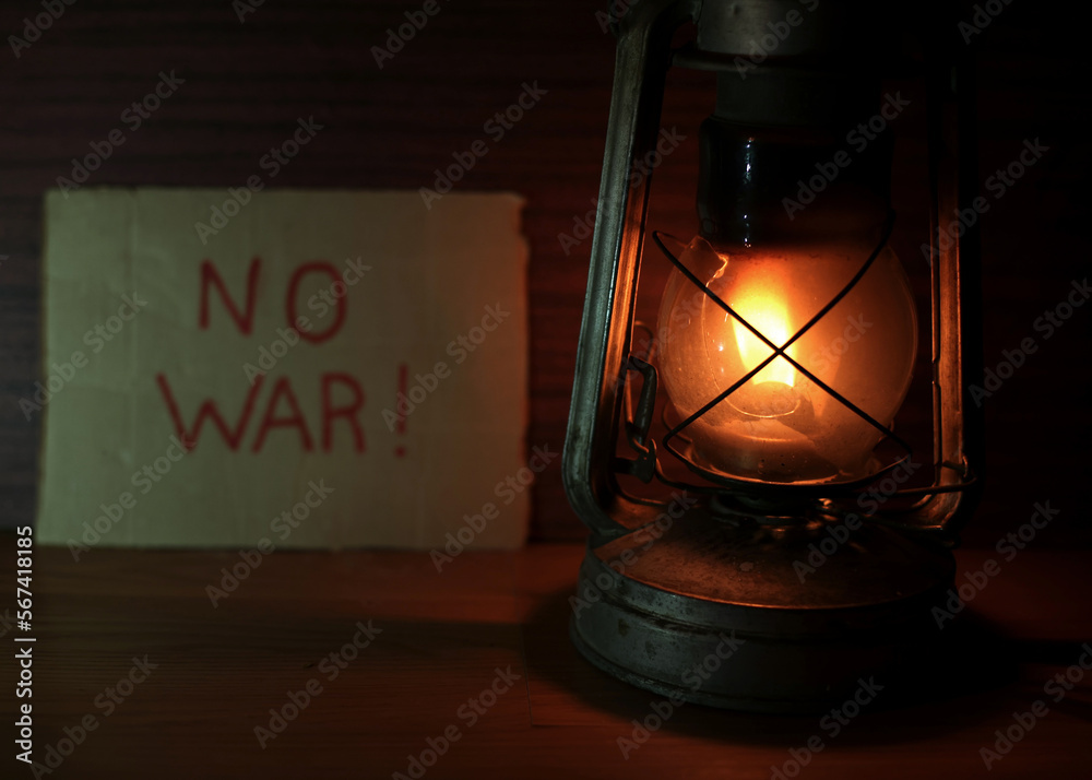 A kerosene lamp, behind the inscription on cardboard, there is no war. Waiting for peace