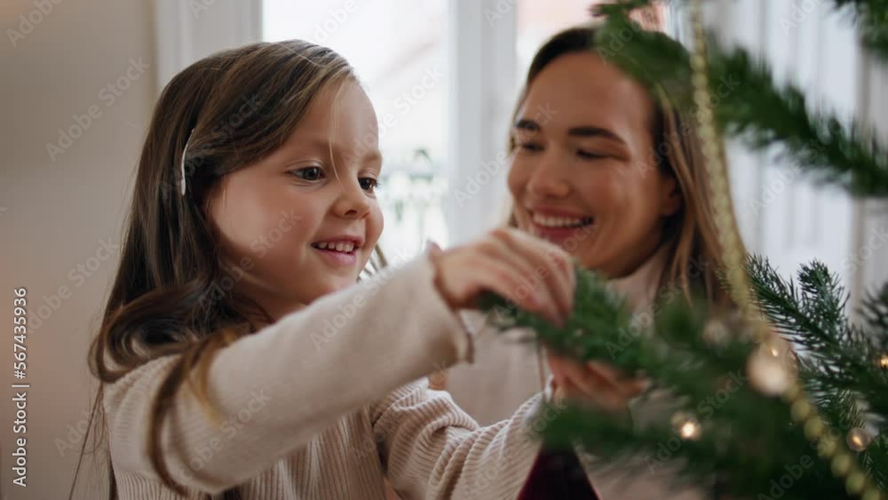 Cute child decorating Xmas tree with mom home closeup. Mother embracing daughter Cute child decorating Xmas tree with mom home closeup. Mother embracing daughter