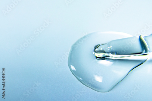 Water bubbles with cosmetic liquid drops of serum on a blue background of a laboratory glass pipette. Close-up of a pipette.