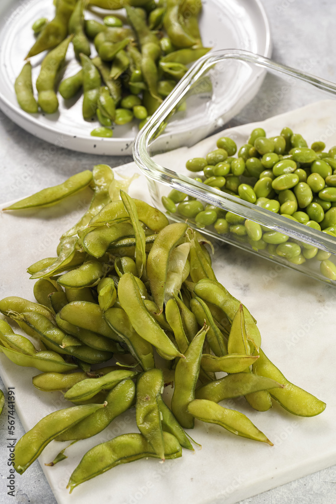 Peeling fresh steamed green soy beans edamame. Japanese plant snack on marble board on light grey background Peeling fresh steamed green soy beans edamame. Japanese plant snack on marble board on light grey background