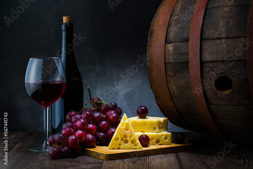 Red wine in low light with cheese and grape,wine barrel and glass